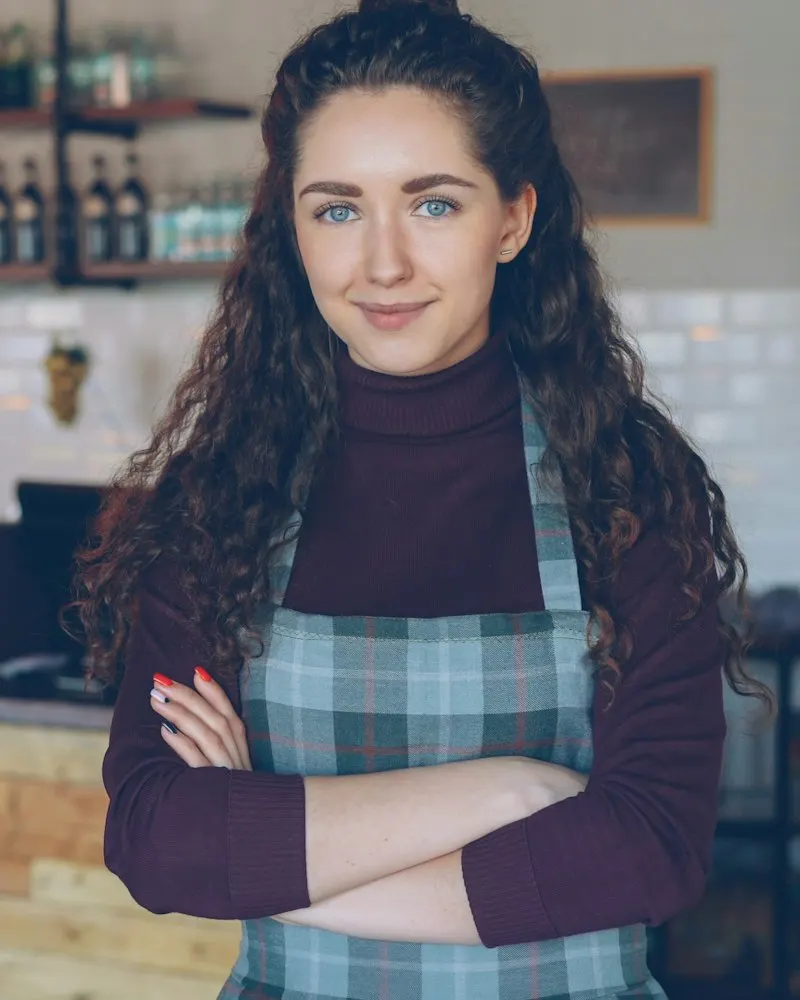 Dueña de una cafetería sonriendo con los brazos cruzados frente a su mostrador